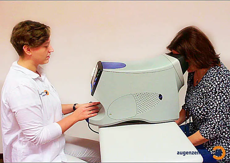 GDx Untersuchung Patientin mit dem Kinn im Stützbügel am GDx Laser-Scanning-Polarimeter, während die Optometristin das Gerät justiert, um die Dicke der Nervenfaserschicht im Auge zu messen.
